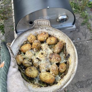 Parmesan and green bean potatoes in an enameled skillet in front of the pizza oven they were cooked in