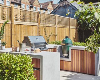 a u shape outdoor kitchen with a green grill and timber cabinets