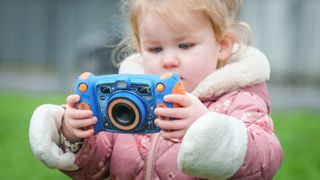 Small girl holding VTech kids' camera outdoors