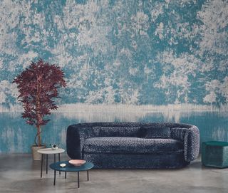 blue wall mural in living room with blue velvet textured sofa, coffee tables, concrete floor