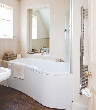 bathroom with cream tile wall bathtub mirror and wooden flooring