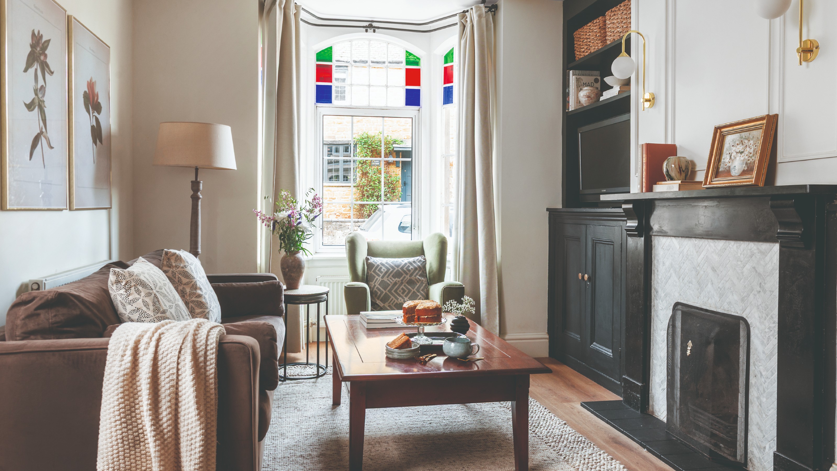 A small living room with a brown sofa, a green armchair and a built-in shelving painted black matching the fireplace