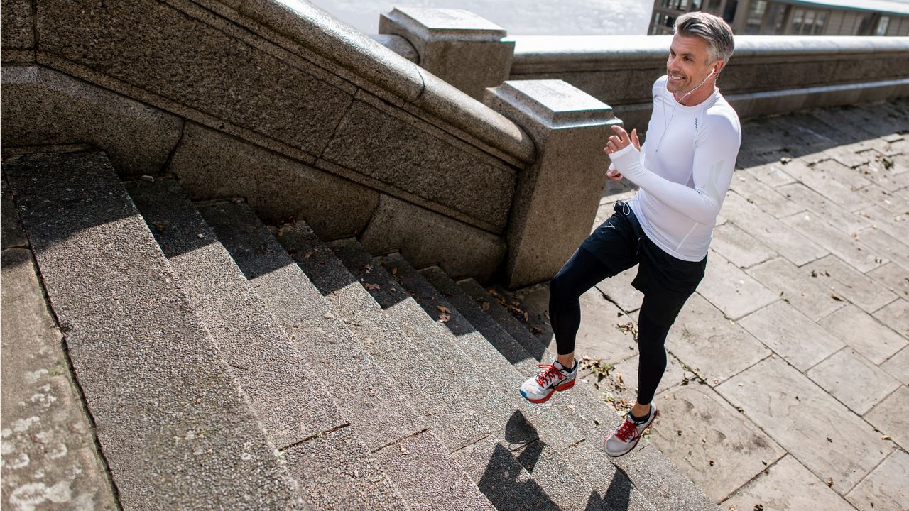 A man smiles as he runs up steps at a riverfront.