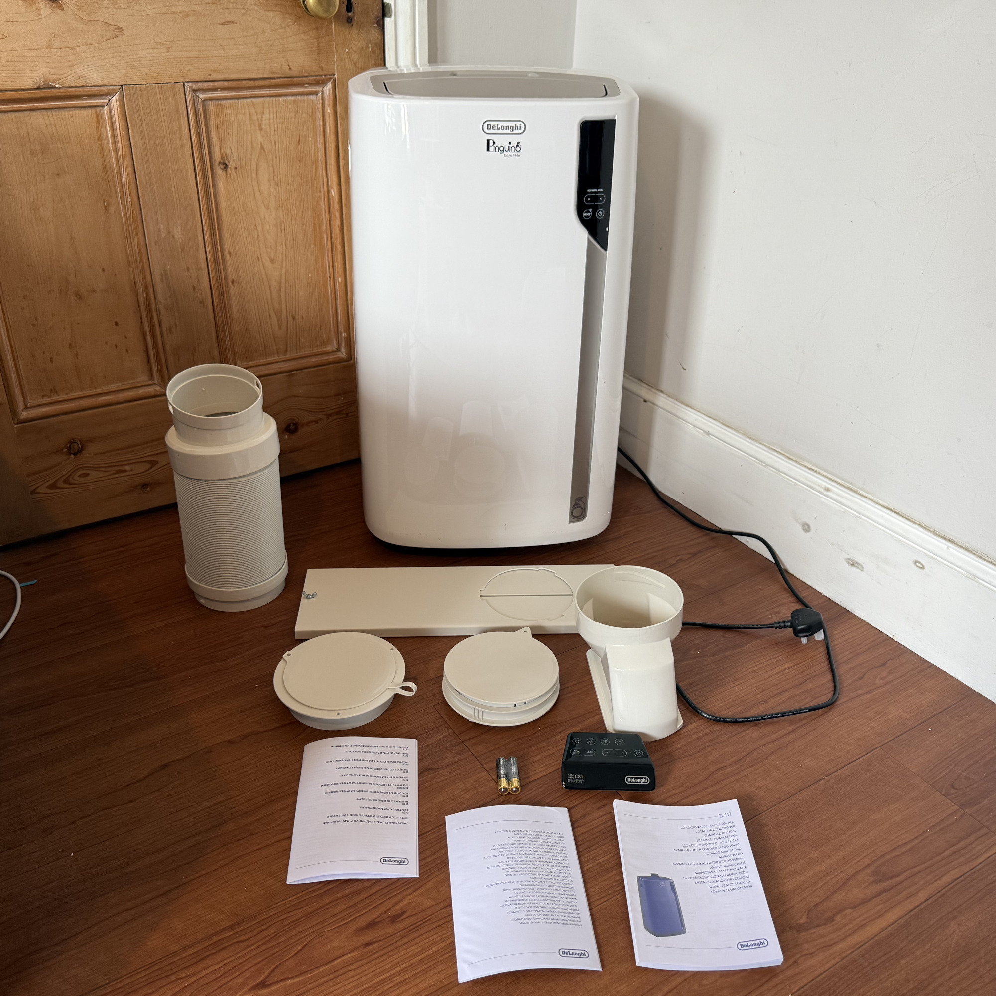delonghi pinguino care4me portable air conditioner and accessories on a wooden floor by a door
