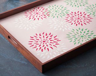A wooden breakfast tray decorated with pale pink paint and an assortment of floral stencil designs in magenta pink, green and white