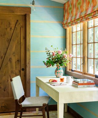 desk in front of window with orange patterned blind and blue and yellow striped wall