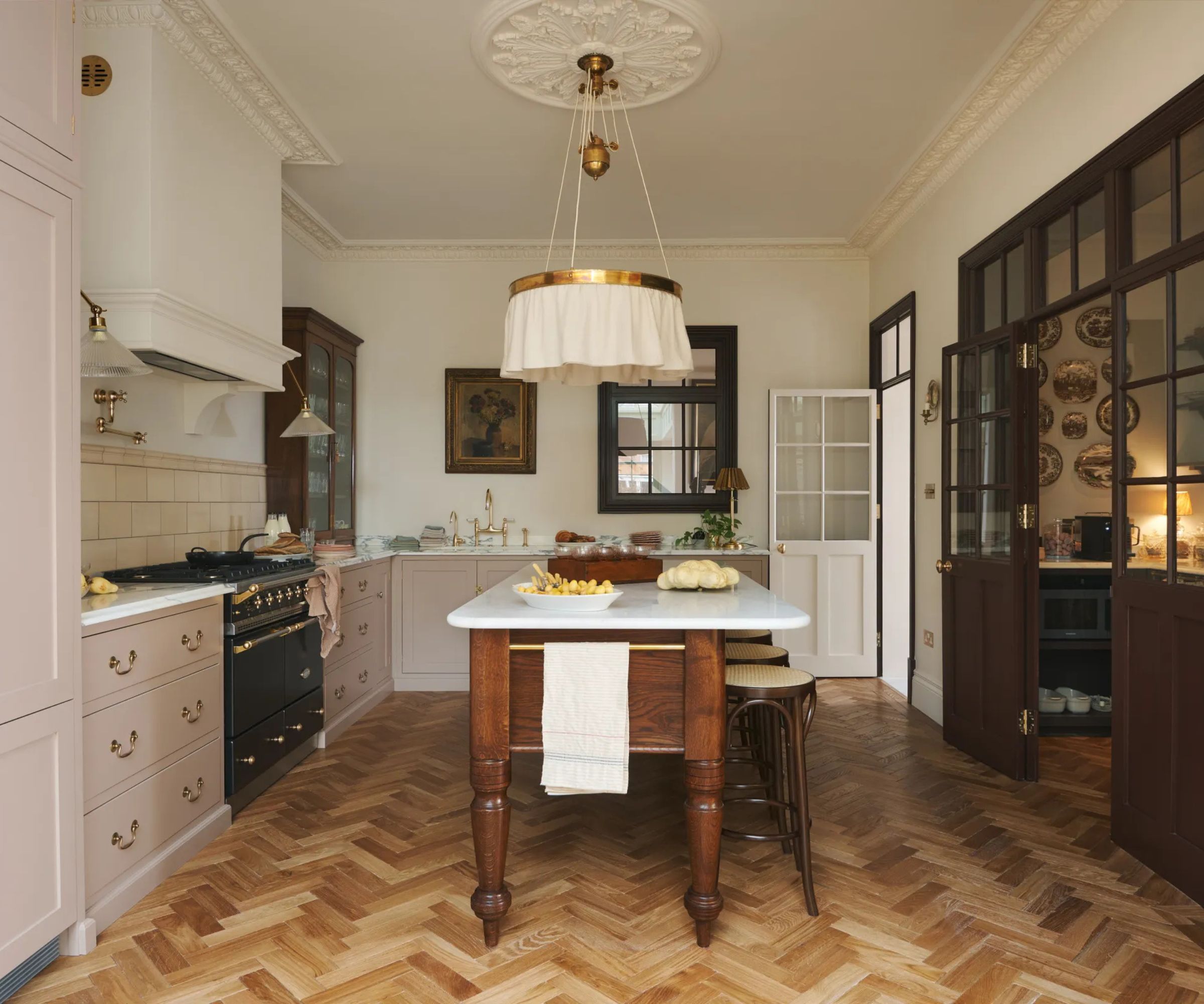 A pink and white kitchen with a large pantry seen through glass doors