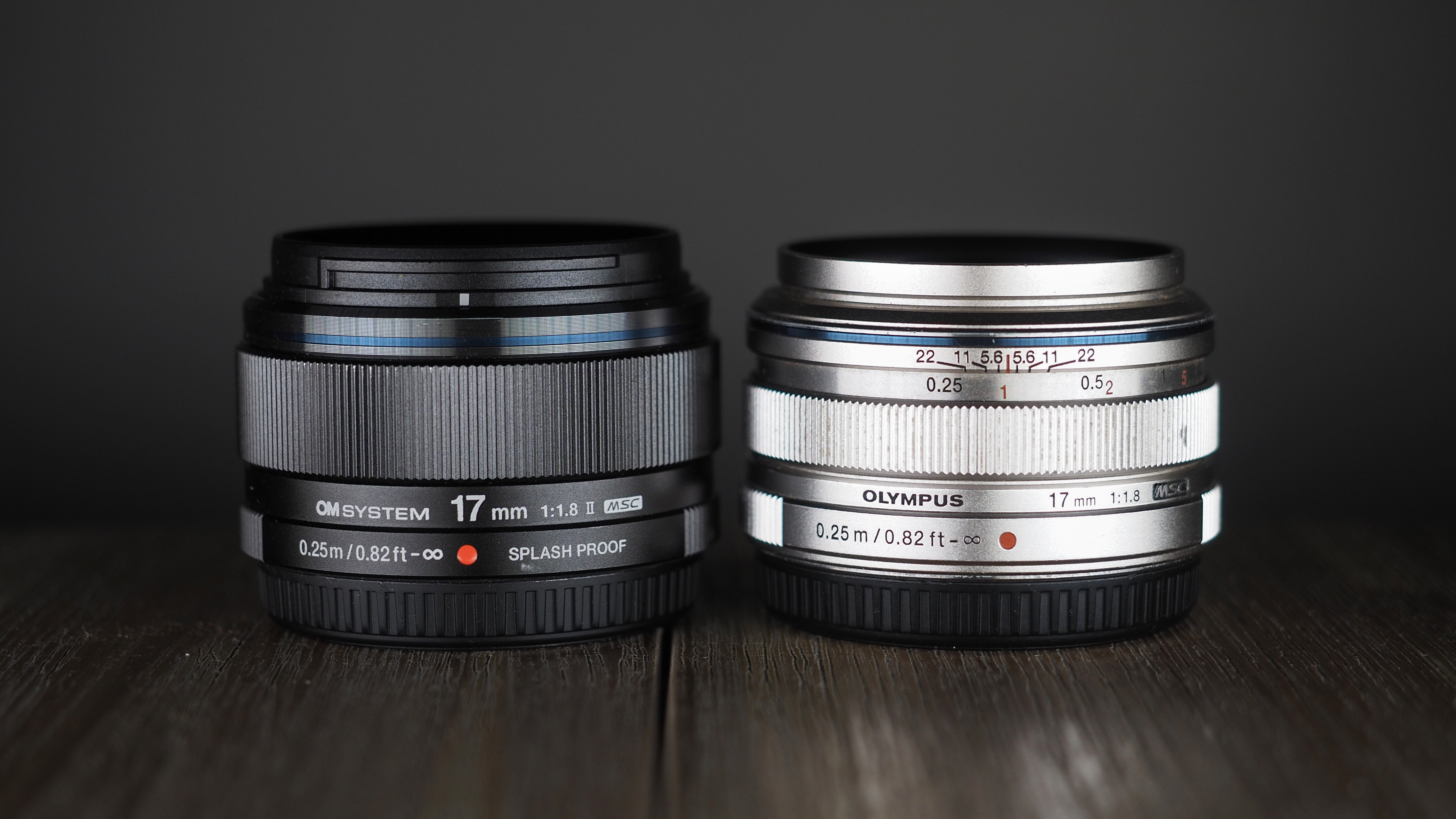 OM System M.Zuiko 17mm f/1.8 II next to an Olympus M.Zuiko 17mm lens on a wooden surface