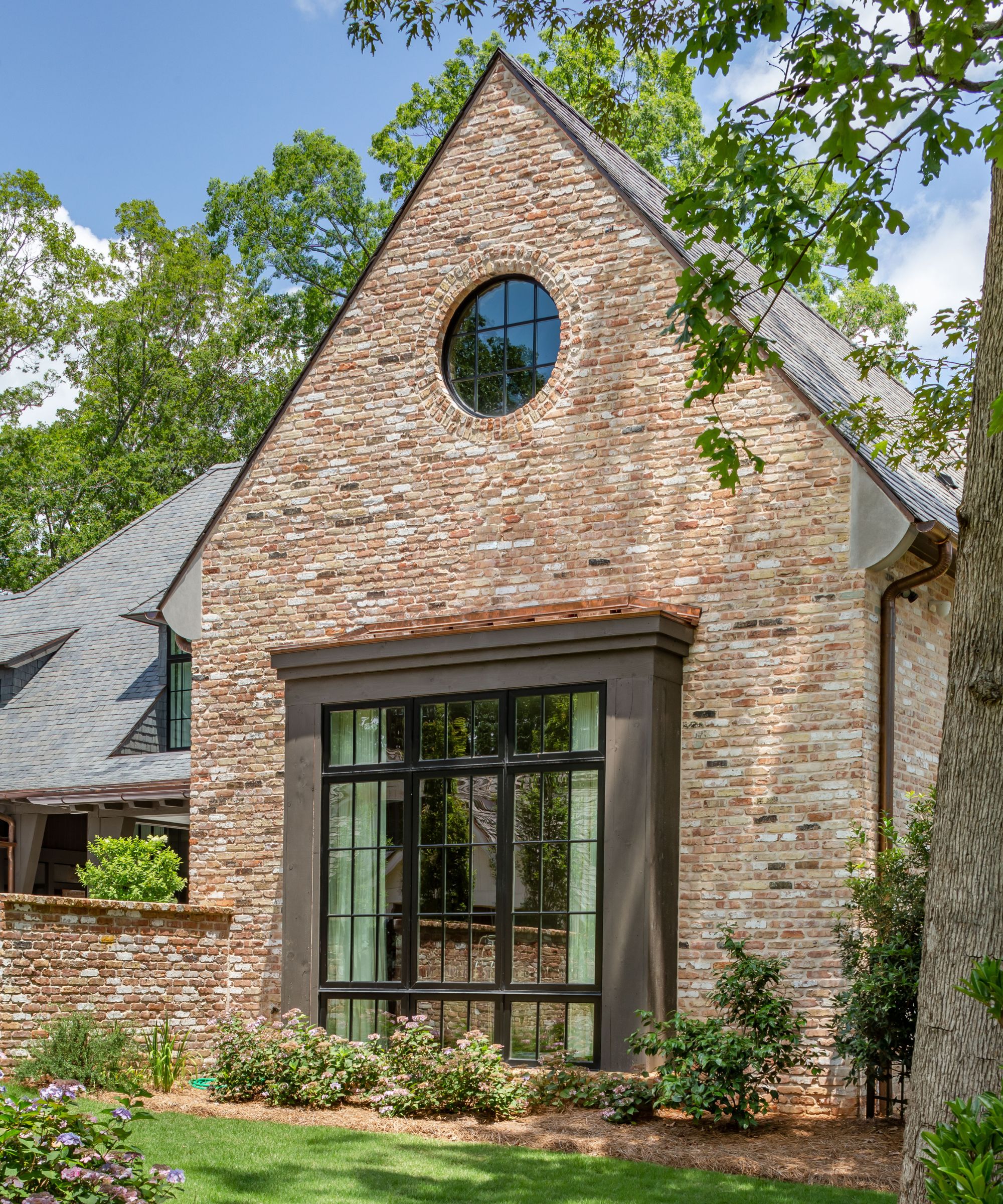 A red brick home exterior with dark brown window trim and a small circular mirror on the upper floor.