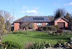 A red house with solar panels on the roof and a lush landscape.