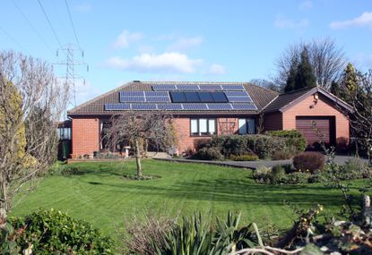 A red house with solar panels on the roof and a lush landscape.