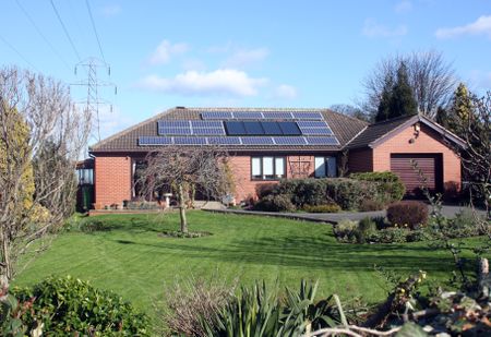 A red house with solar panels on the roof and a lush landscape.