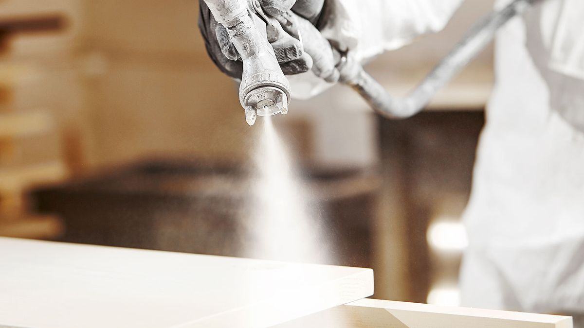 Paint sprayer spraying white paint on kitchen cabinet door