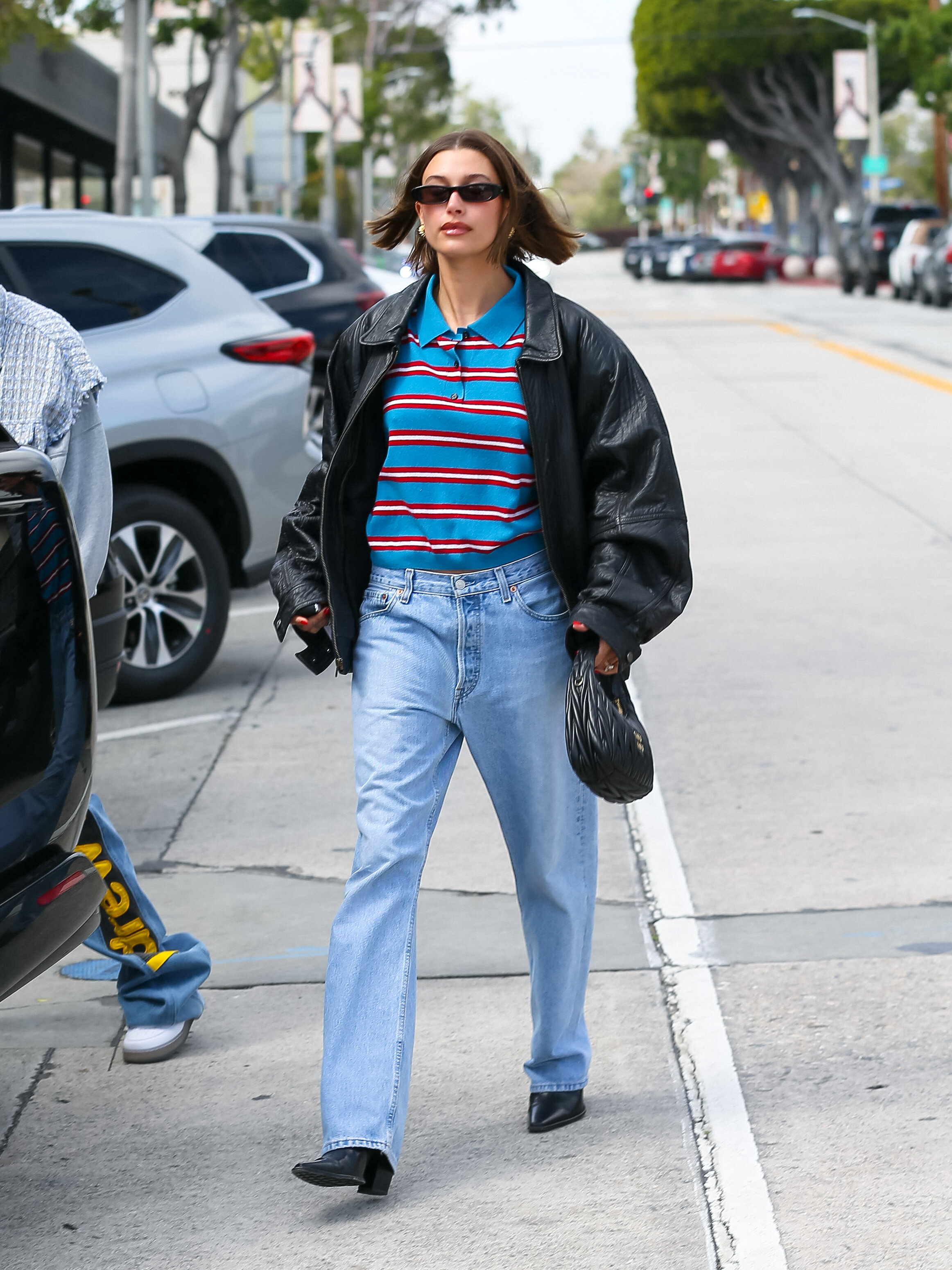 Hailey Bieber in Levi jeans, a striped polo sweater, and a leather bomber jacket.