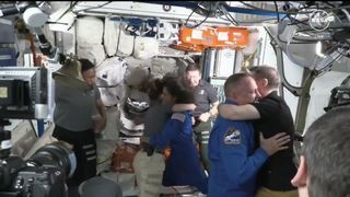 Seven astronauts float in a mostly-white module of a space station, hugging and smiling. Suni Williams and Butch Wilmore are embraced aboard the ISS as they enter from their Starliner spacecraft June 6, 2024.
