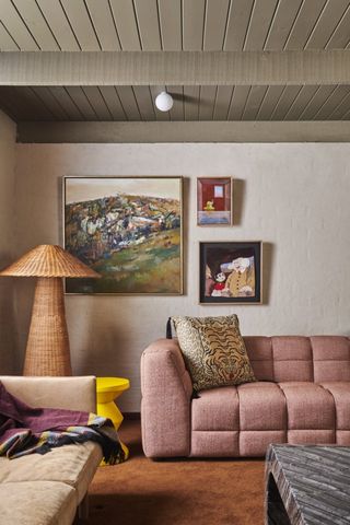 modern boho style living room with pink sofa, rattan floor lamp, tiger print pillow, yellow stool, and orange floor rug