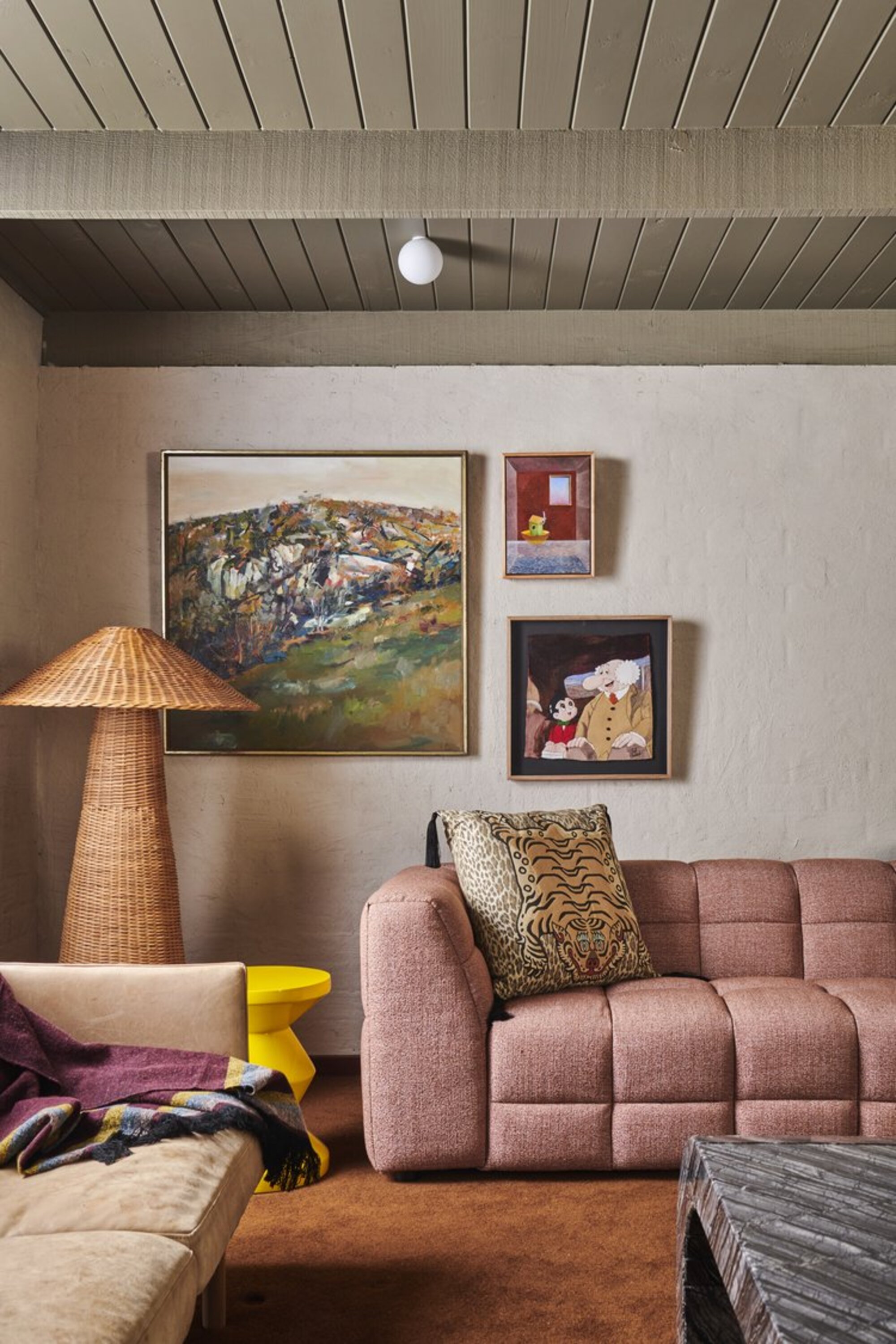 Living room in a modern boho style with pink sofa, rattan -floor lamp, tiger pressure pillow, yellow stool and orange floor carpet