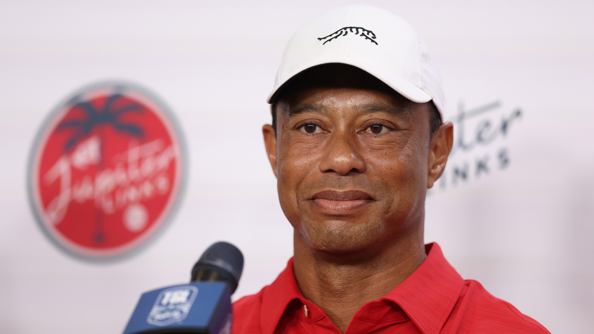 Tiger Woods speaks to the media at TGL wearing a white cap and red polo
