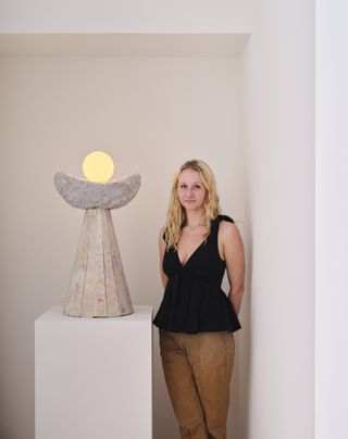 A portrait of designer Susannah Weaver alongside a lamp she designed, photographed at Carpenters Workshop Gallery