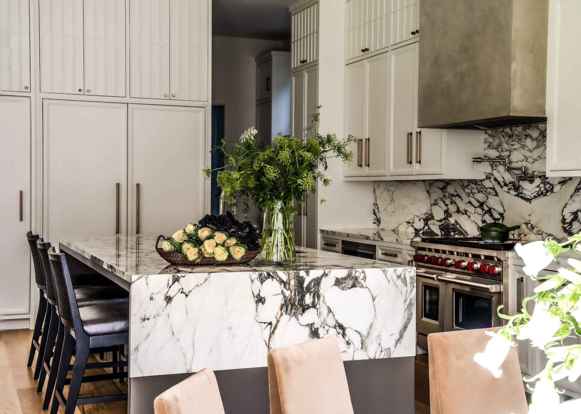 A neutral off-white kitchen with floor to ceiling cabinetry and a large island covered in a bold marble