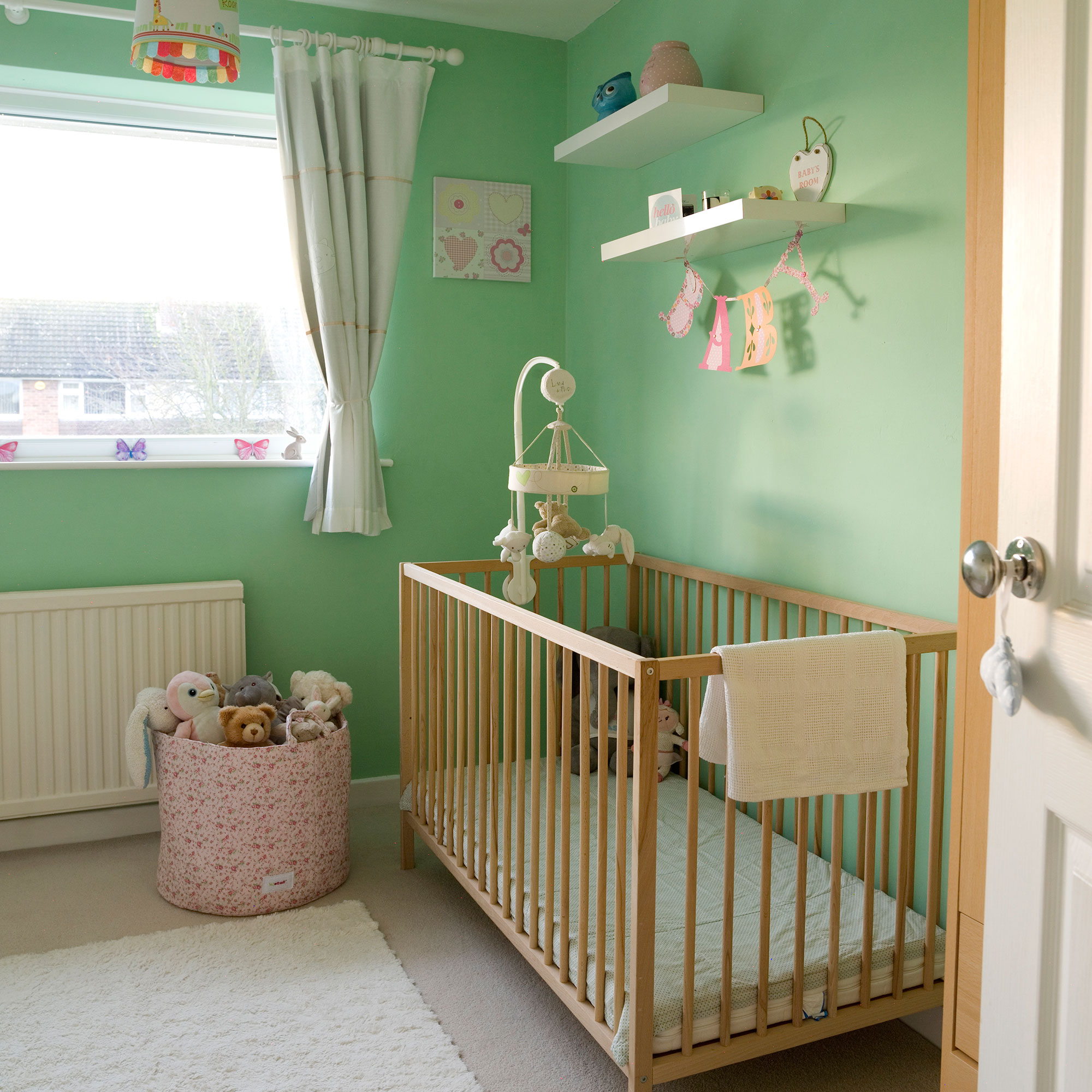 Green nursery with warm wood cot and mobile above cot