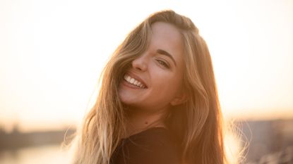 Woman posing sideways, sunset background.