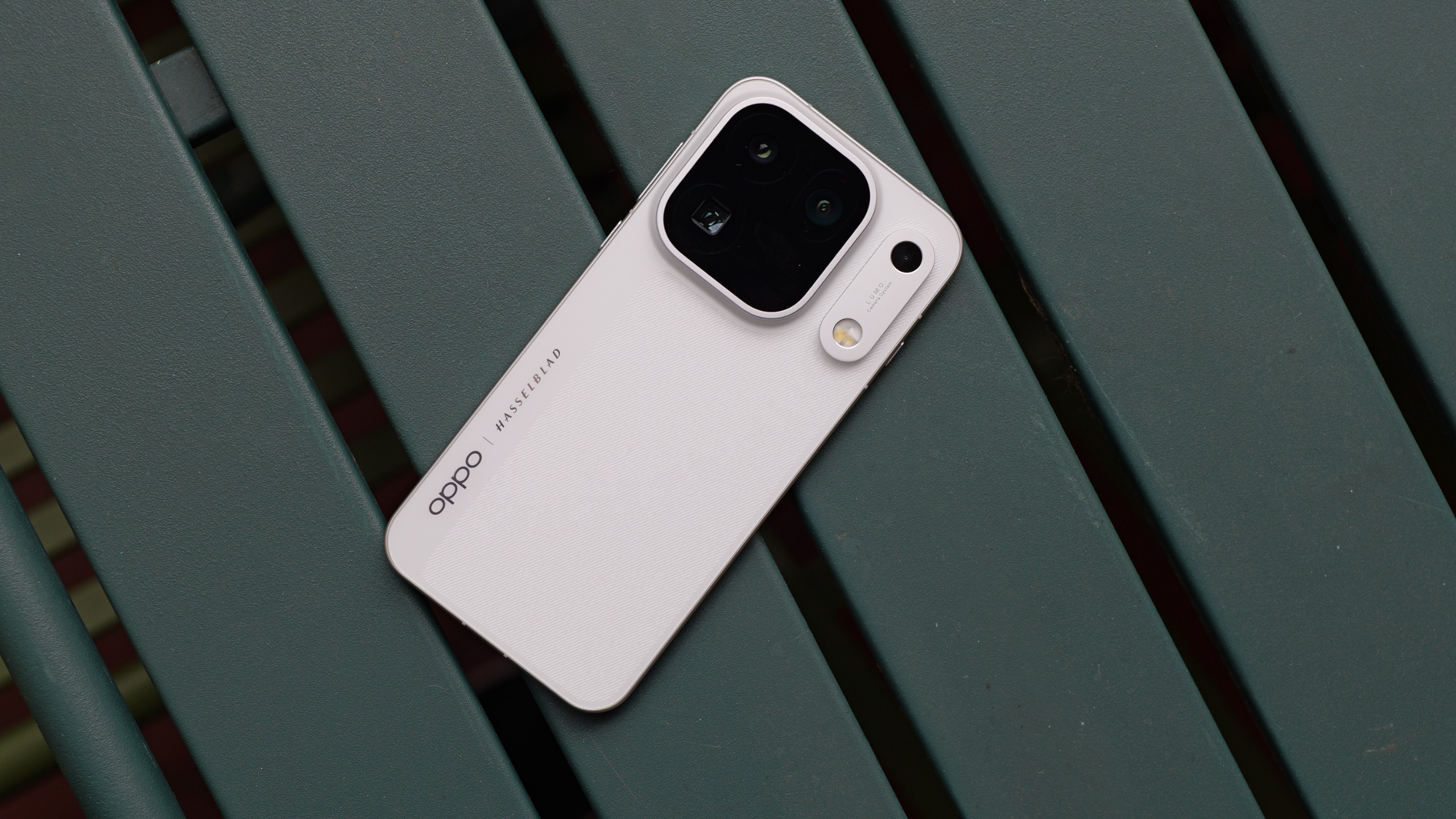 White Oppo Find X10 Pro Max resting diagonally across a dark green slatted bench, showing the textured rear panel and camera module.