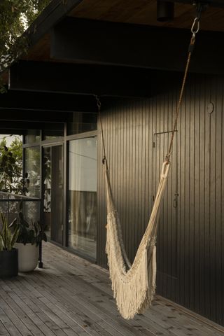 A deck with dark gray siding and a macrame hanging seat