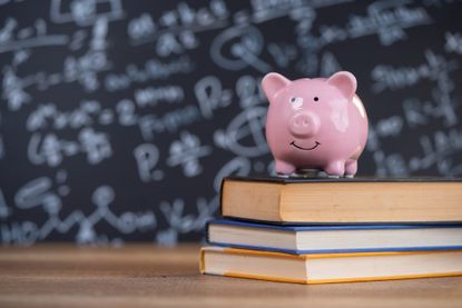 pink piggy bank placed on top of three stacked books with a chalkboard in the background