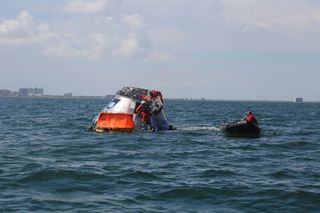 An astronaut exits the Orion space capsule in the Gulf of Mexico during an emergency-egress test on July 11, 2017. The orange raft to the left is their lifeboat.  