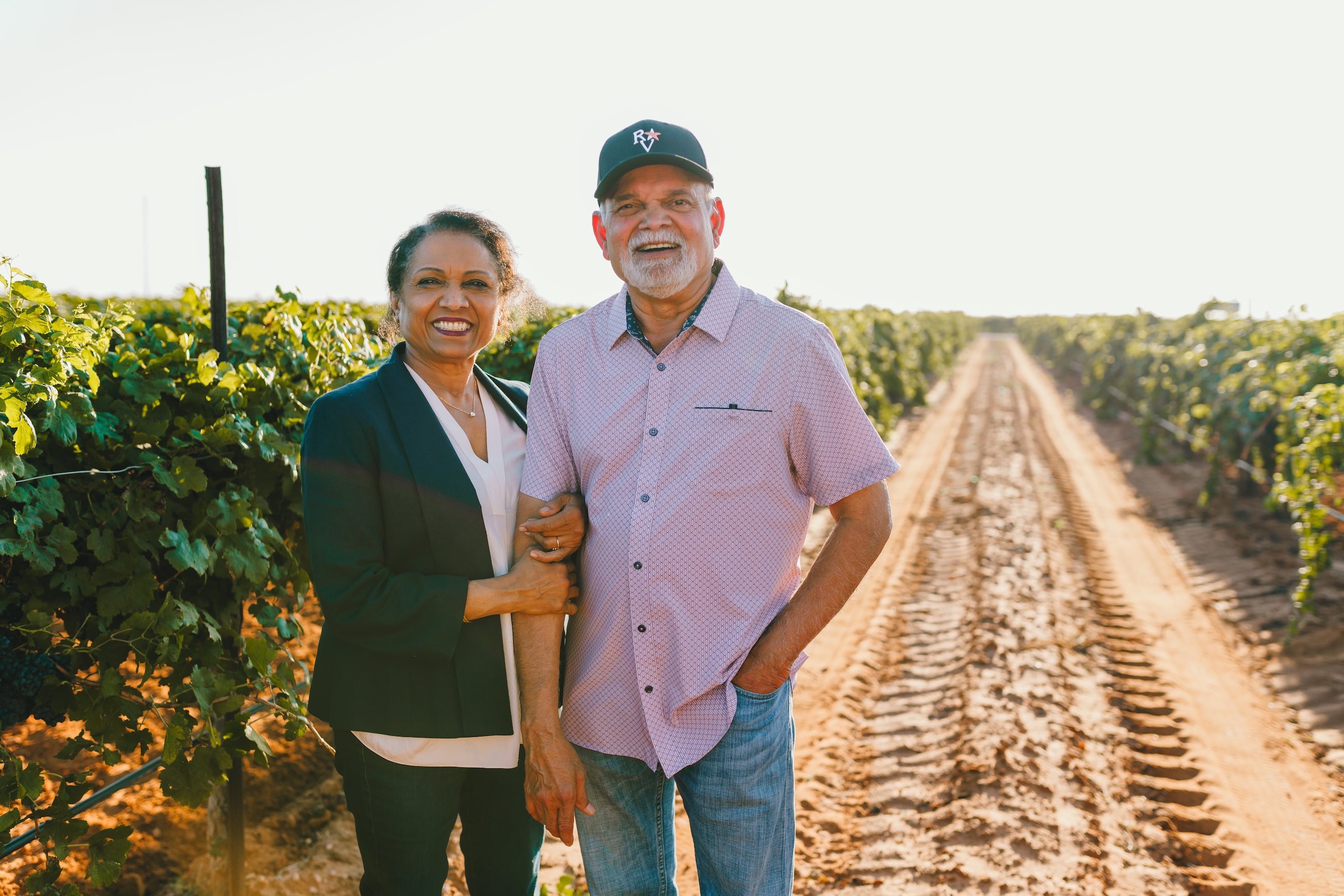 The owners of Reddy Vineyards standing in a vineyard, with tractor tracks stretching along a dirt row between the vines