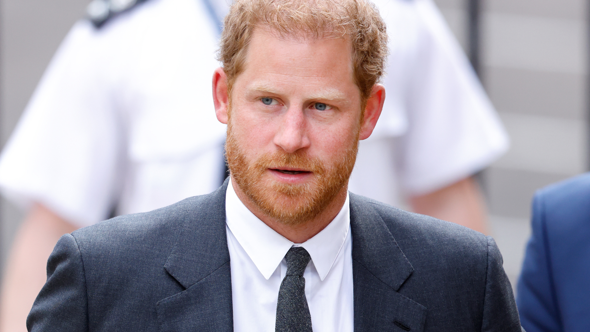 Prince Harry has red hair and a red beard and wears a navy suit and tie