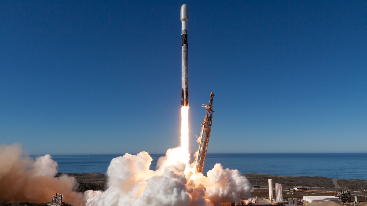 a black and white rocket launches into a blue sky from a seaside pad