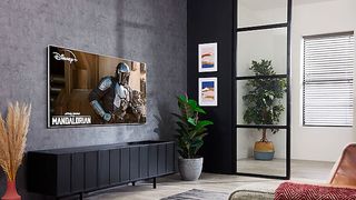 The Samsung QN85A Neo QLED TV in a grey room on media unit showing the mandalorian