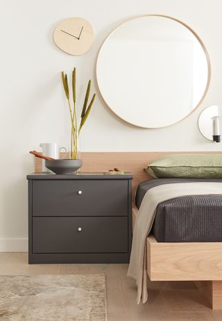 Bedroom mirror above side table with neutrally colored bedroom plus dark gray accents and natural wooden furnishings