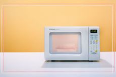 A microwave on a white table with a yellow background
