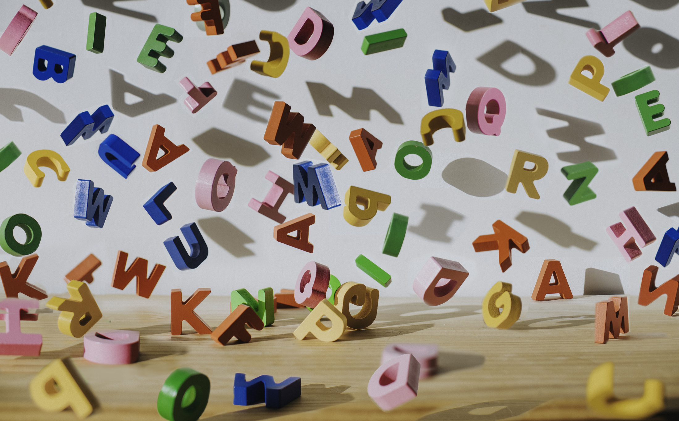 Conceptual image of colorful falling letters, casting shadows on a white wall.