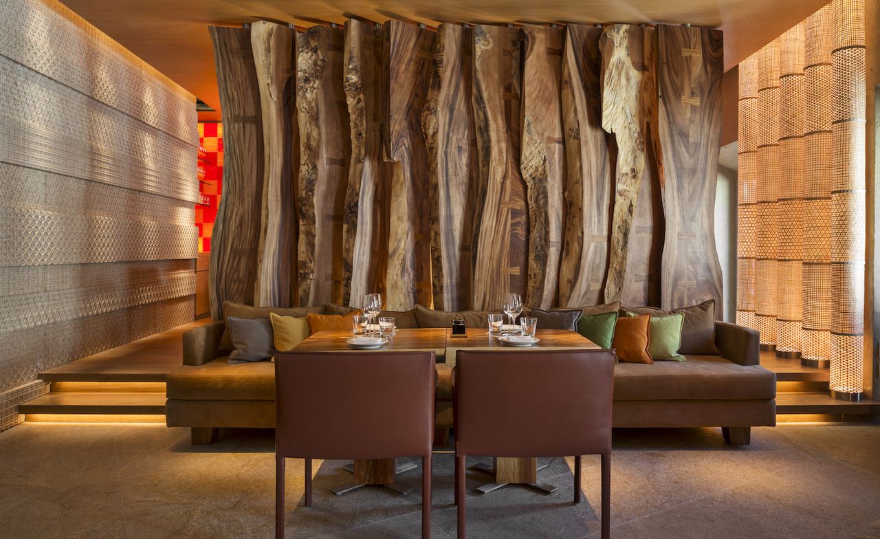 A dining area with a decorated table, with leather chairs on one side and a long sofa on the other against a wall made from natural wood slats.