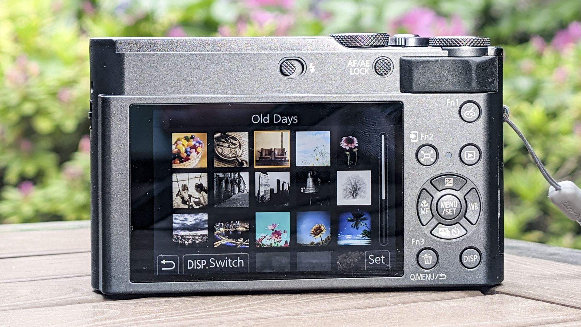 Panasonic Lumix TZ300 compact camera's rear screen on a wooden table, with a colorful floral backdrop