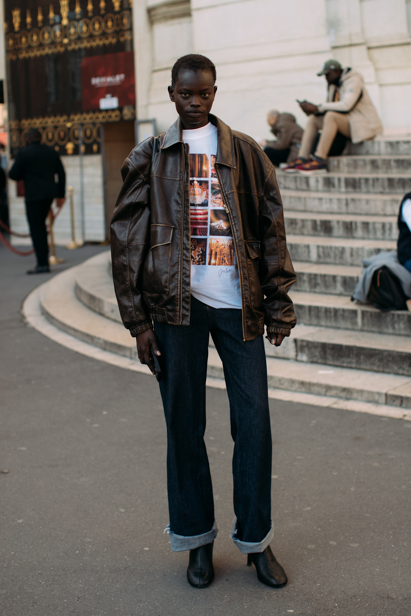 fashion week attendee wearing brown leather jacket, graphic tee, jeans, and black boots