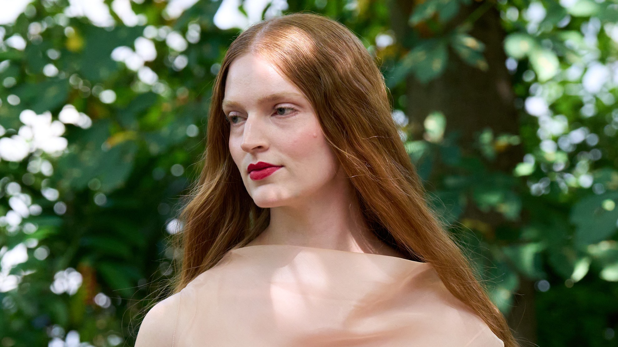woman with red hair wearing a nude top in front of a tree