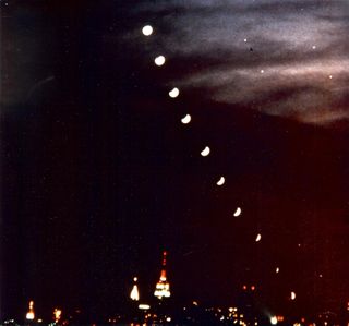 This composite image of the total lunar eclipse of December 30, 1982, was taken by Night Sky columnist Joe Rao. The montage of ten images of the moon, gradually becoming immersed in the Earth's shadow were taken at six minute intervals on a single frame of Kodak High Speed Extachrome film from Jones Beach, Long Island, NY. Note the double images of the stars Pollux and Castor, of Gemini, the Twins in the upper right part of the photograph. The day after the eclipse, Rao went to Ferry Point Park in the Bronx, where he photographed the Manhattan skyline. He then superimposed that image with the eclipse montage.