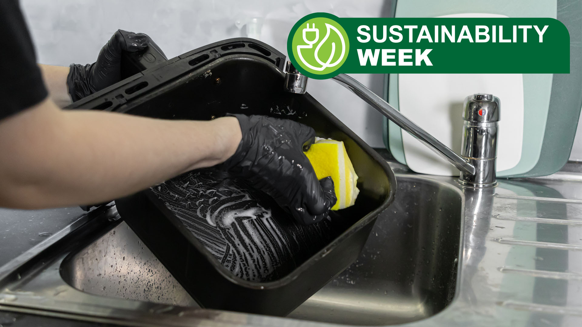 Person wearing black gloves washing air fryer basket in kitchen sink