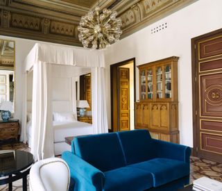 a guest room at the Cotton House Hotel in Barcelona features a white bed canopy and blue sofa