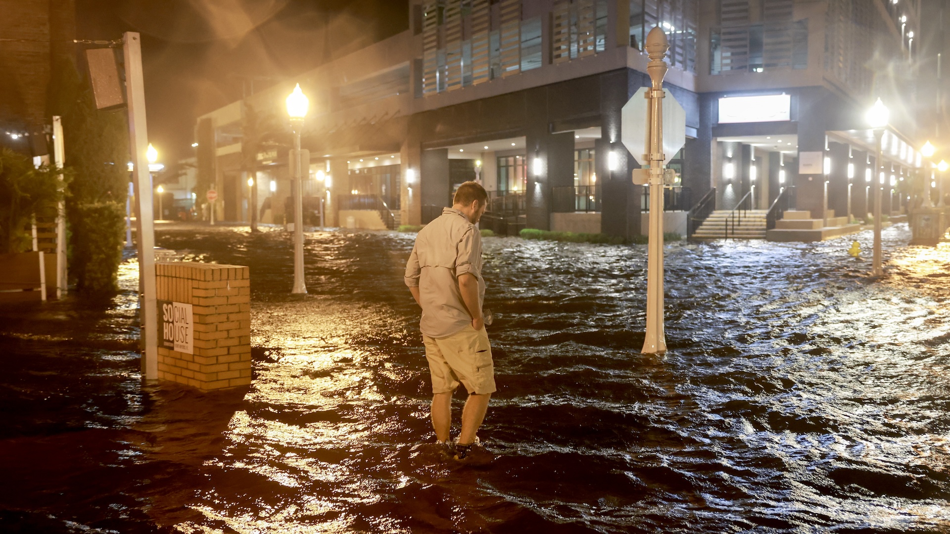 A man walks through a flooded city street at night with water up to his ankles