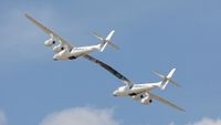 two white aircraft joined together as one at the wing fly through a blue sky