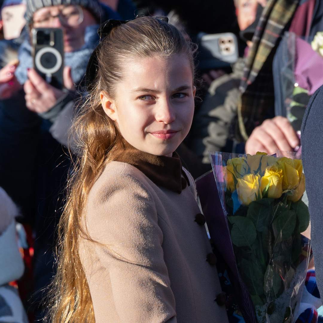 Princess Charlotte wears a light brown coat on Christmas Day in 2025 and is handed yellow and red flowers by royal fans in Sandringham