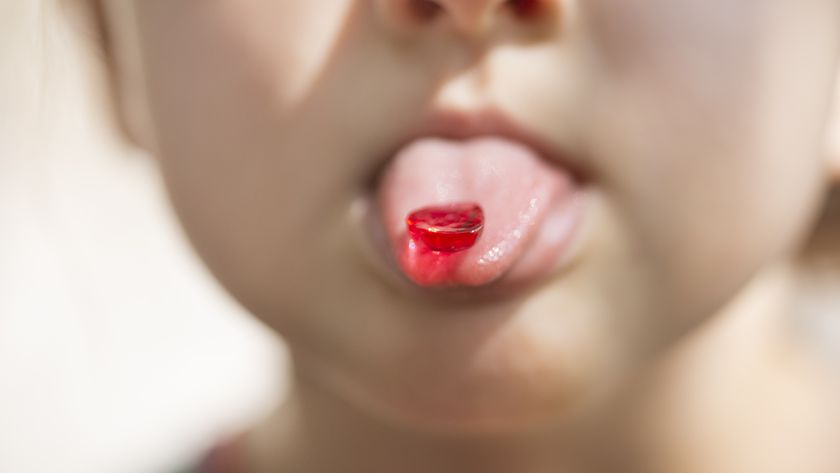 a child sticks out their tongue with a red candy gummy on it