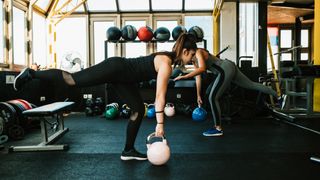 Two women perform the single-leg Romanian deadlift in a gym with a kettlebell