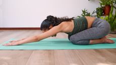 A woman doing yoga child's pose in a room lined with leafy plants